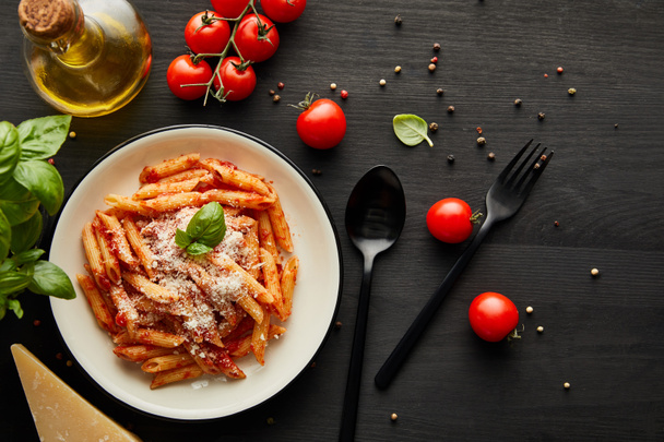 top view of tasty bolognese pasta with tomato sauce and Parmesan in white plate near ingredients and cutlery on black wooden background - Φωτογραφία, εικόνα
