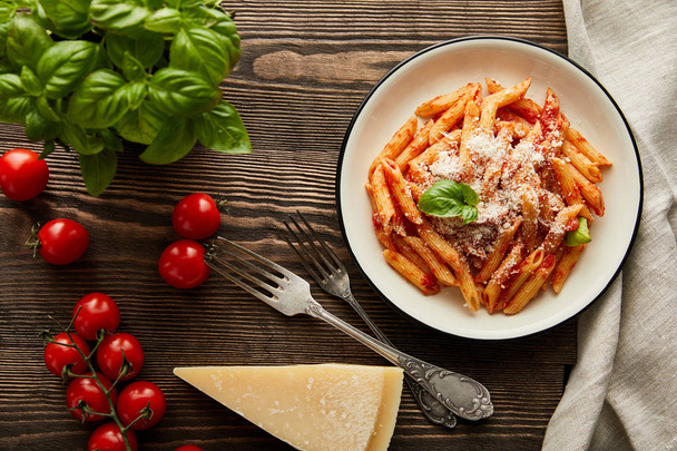 bovenaanzicht van lekkere bolognese pasta met tomatensaus en Parmezaanse kaas in wit bord bij ingrediënten en bestek op houten tafel - Foto, afbeelding