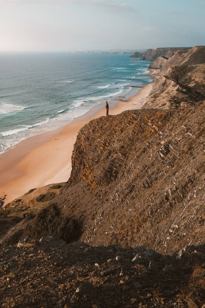 Vertical shot of a person on a cliff looking at the beautiful ocean in Algarve, Portugal - Foto, imagen