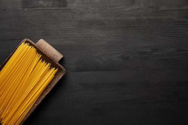 top view of raw spaghetti on black wooden background - Zdjęcie, obraz