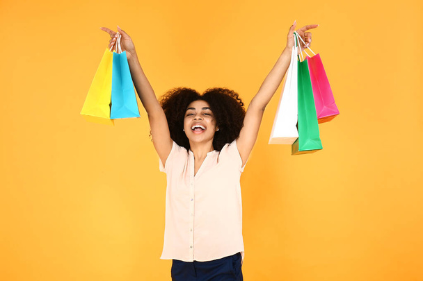 Krásná afroamerická žena s nákupními taškami na barevném pozadí - Fotografie, Obrázek