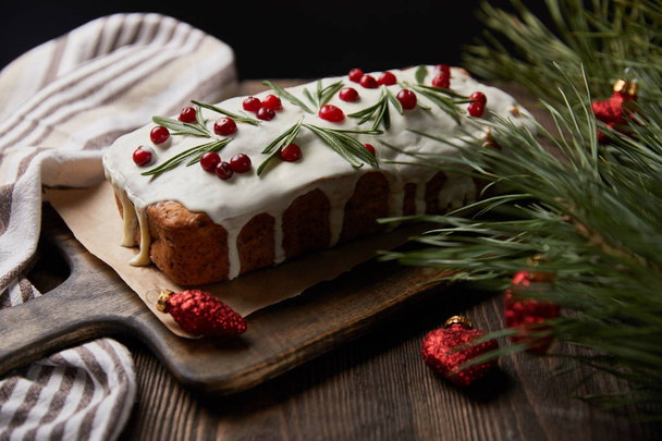 traditional Christmas cake with cranberry near pine branch with red baubles and napkin on wooden table isolated on black - Фото, зображення