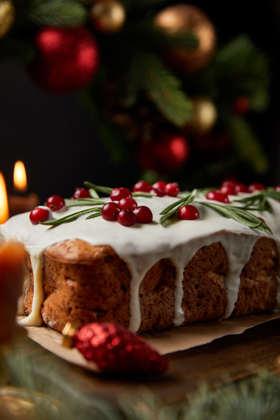 selective focus of traditional Christmas cake with cranberry near burning candles, Christmas wreath with baubles on wooden table - Φωτογραφία, εικόνα