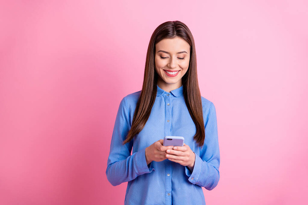 Photo of cheerful nice cute charming student holding smartphone with her hands browsing through media resources smiling toothily isolated over pink pastel color background - Zdjęcie, obraz