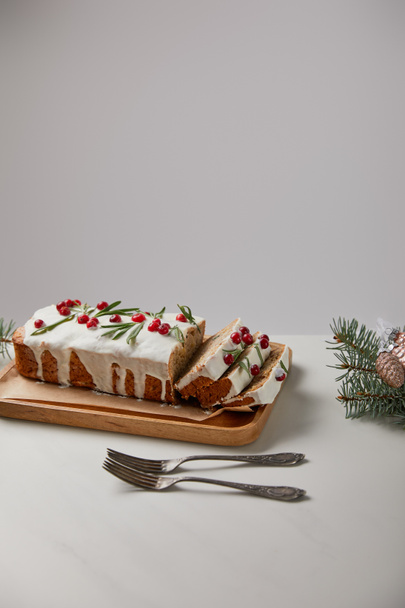 traditional Christmas cake with cranberry near forks, baubles and pine on white table isolated on grey - Фото, зображення