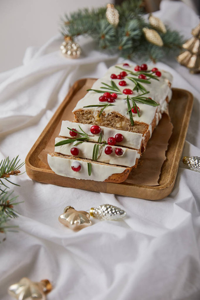 selective focus of traditional Christmas cake with cranberry on wooden board near baubles and pine on white cloth isolated on grey - Фото, изображение