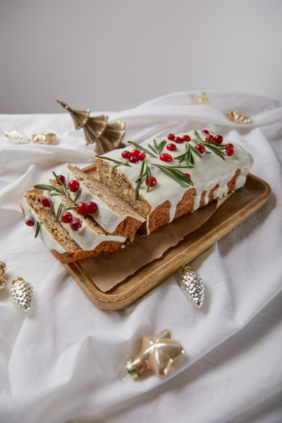 traditional Christmas cake with cranberry on wooden board near baubles on white cloth isolated on grey - Foto, imagen