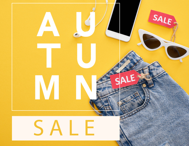 vista dall'alto di jeans, occhiali e smartphone con auricolari con etichette di vendita su sfondo giallo con illustrazione vendita autunno
  - Foto, immagini