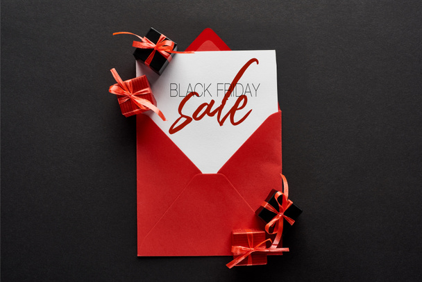 Ansicht der Karte mit Abbildung zum Black Friday Sale in rotem Umschlag in der Nähe von Geschenken auf schwarzem Hintergrund - Foto, Bild