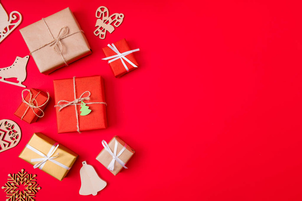 Photo of creative conept of presents wrapped among new year items like bells skates and snowflakes near copyspace isolated vibrant color red background - Foto, imagen