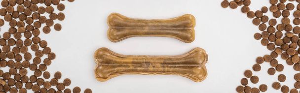 vrchní pohled na suché krmivo pro domácí mazlíčky roztroušené kolem kostí izolovaných na bílém panoramatickém snímku - Fotografie, Obrázek