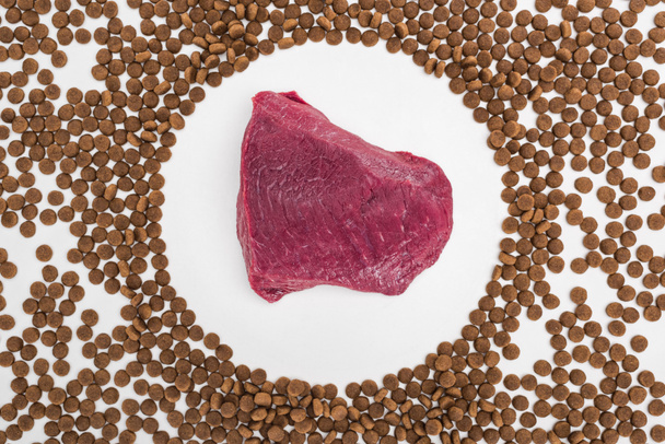 верхний вид сухой корм для домашних животных разбросаны по сырому мясу изолированы на белом
 - Фото, изображение