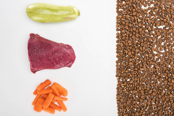 flat lay with dry pet food near raw meat, carrot and zucchini isolated on white - 写真・画像