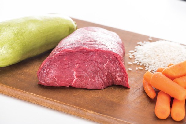 raw meat, rice, carrot and zucchini on wooden cutting board isolated on white - 写真・画像