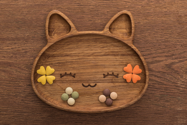 top view of feline dry pet food and vitamins in cute cat shape plate on wooden table - Fotó, kép