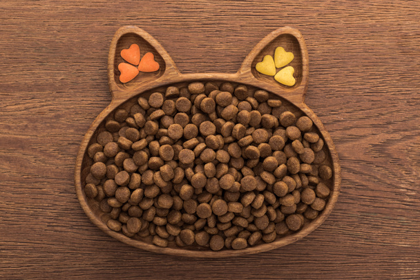 верхний вид кошачьего сухого корма и витаминов в форме кошки на деревянном столе
 - Фото, изображение