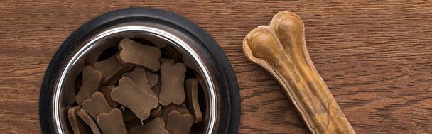 top view of dry pet food in silver bowl near bone on wooden table, panoramic shot - Фото, зображення