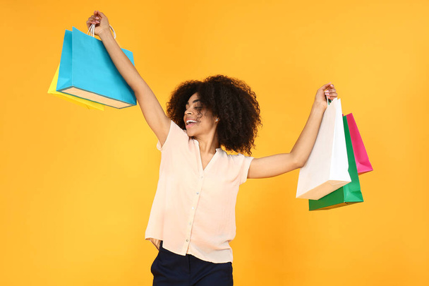 Beautiful African-American woman with shopping bags on color background - Фото, зображення