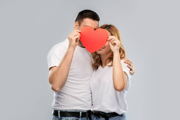 smiling couple hiding behind big red heart - Фото, изображение