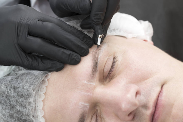 Procedimiento de tatuaje de cejas Microblading en un salón de belleza para hombres
 - Foto, imagen