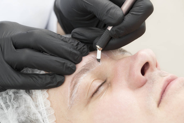 Microblading procedimento da tatuagem da sobrancelha em um salão de beleza para homens
 - Foto, Imagem