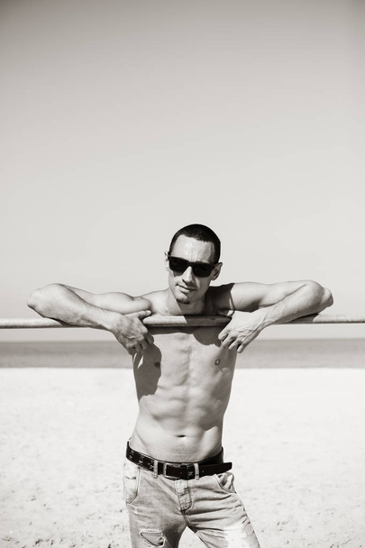 junger muskulöser Mann, der sich ausruht und am Strand posiert. mit Sonnenbrille - Foto, Bild