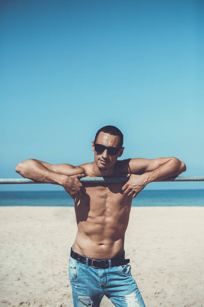 jovem homem musculoso descansando e posando na praia. Usar óculos escuros
 - Foto, Imagem