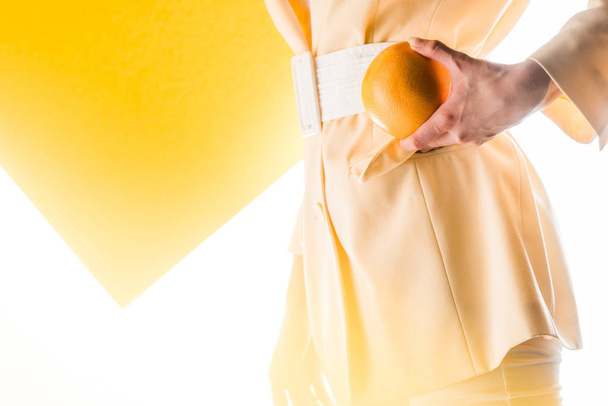 cropped view of stylish woman holding orange on white and yellow  - Фото, изображение