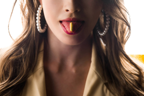 Ausgeschnittene Ansicht einer Frau, die mit gelber Pille auf weißer Zunge die Zunge herausstreckt  - Foto, Bild
