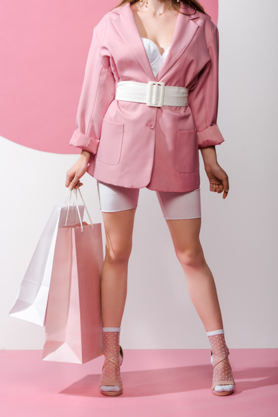 cropped view of stylish girl holding shopping bags on white and pink  - Foto, afbeelding