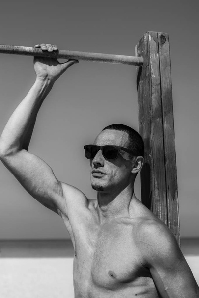 young muscular man resting and posing on the beach. Wearing sunglasses - Foto, afbeelding