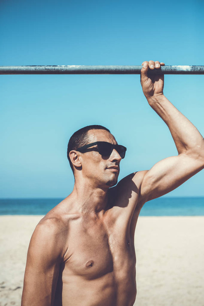 young muscular man resting and posing on the beach. Wearing sunglasses - Fotó, kép