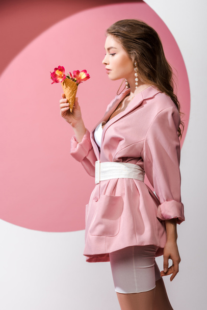 side view of attractive woman looking at ice cream cone with flowers on white and pink  - Photo, Image