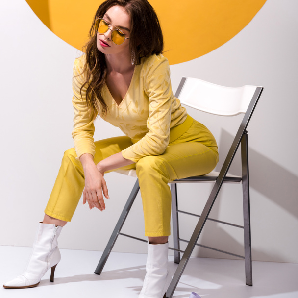 attractive girl in sunglasses sitting on chair on orange and white  - 写真・画像