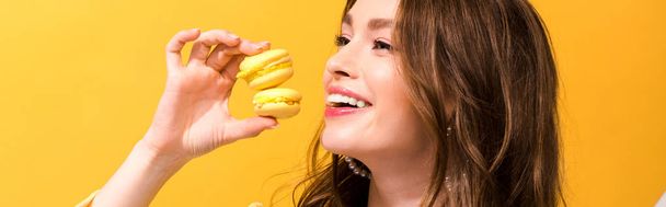 panoramic shot of happy woman holding macarons on yellow - Zdjęcie, obraz