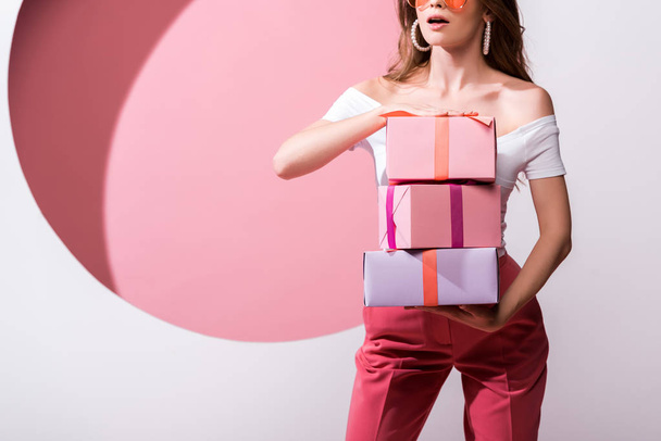 cropped view of surprised woman holding presents on pink and white  - Foto, Bild