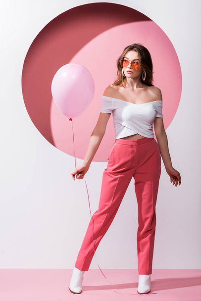 attractive woman holding balloon on pink and white  - Фото, зображення