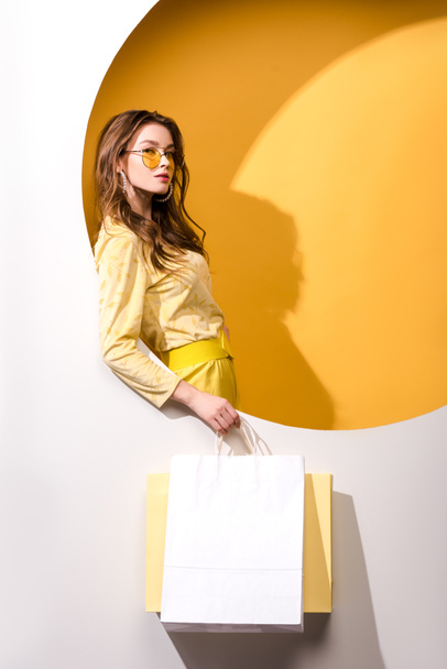 young attractive woman in sunglasses holding shopping bags on orange and white  - Foto, Imagem