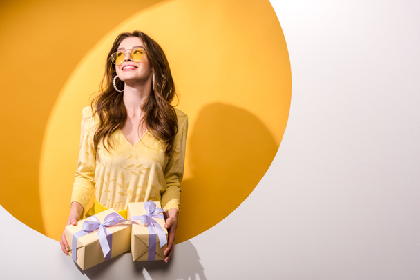 mujer alegre en gafas de sol sosteniendo regalos en naranja y blanco
  - Foto, imagen