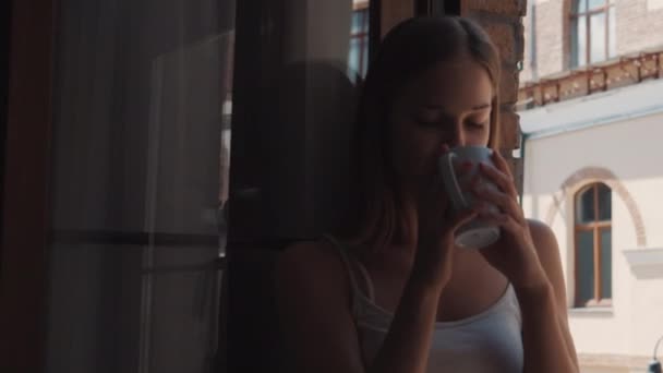 mulher está bebendo café sentado no peitoril da janela e visualização na rua
 - Filmagem, Vídeo