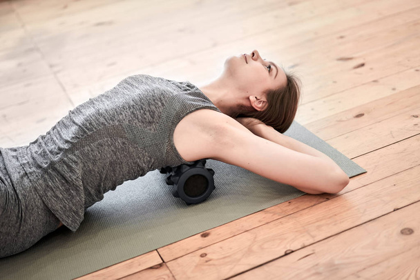 Brunette doing yoga lying on massager on mat on wooden floor in gym - Фото, зображення