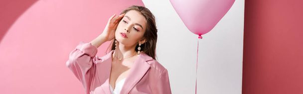 panoramisch schot van aantrekkelijke jonge vrouw houden ballon op roze en wit  - Foto, afbeelding