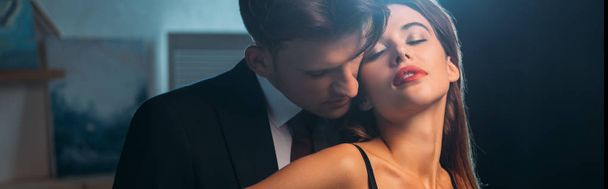 panoramic shot of businessman kissing girlfriend with closed eyes in apartment  - Photo, Image