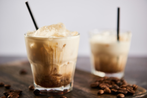 selective focus of white russian cocktail in glasses with straws on wooden board with coffee grains isolated on grey - Φωτογραφία, εικόνα