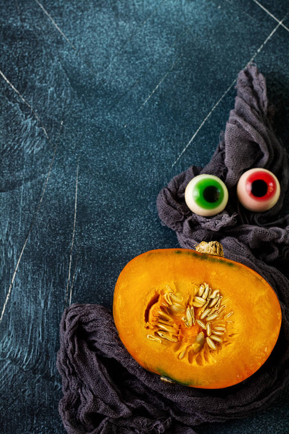 Freshly cut in half pumpkin with gray napkin and Halloween decorations with eyes on old stone dark blue background. Halloween concept. Top view. - Foto, immagini