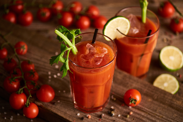 selective focus of bloody mary cocktail in glasses on wooden background with salt, pepper, tomatoes and celery - Photo, Image