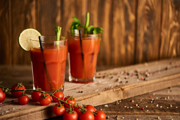 selective focus of bloody mary cocktail in glasses on wooden background with salt, pepper, tomatoes and celery - Photo, Image