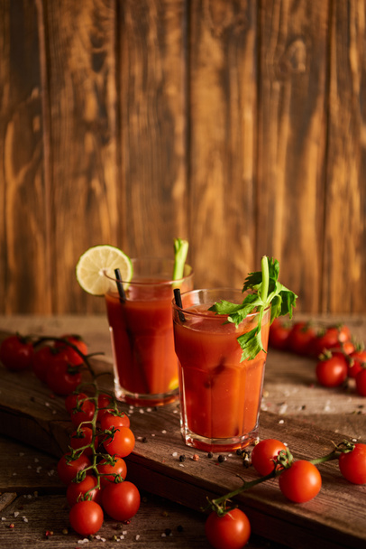 selektiver Fokus des blutigen Cocktails in Gläsern auf hölzernem Hintergrund mit Salz, Pfeffer, Tomaten und Sellerie - Foto, Bild