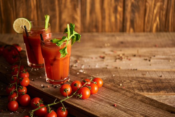 Bloody Mary koktejl v brýlích na dřevěném pozadí se solí, pepřem, rajčaty a celerem - Fotografie, Obrázek