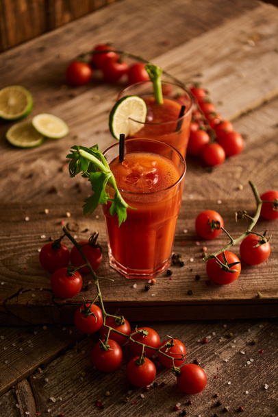 selektivní zaměření Bloody Mary koktejl v brýlích na dřevěném pozadí se solí, pepřem, rajčaty a celerem - Fotografie, Obrázek